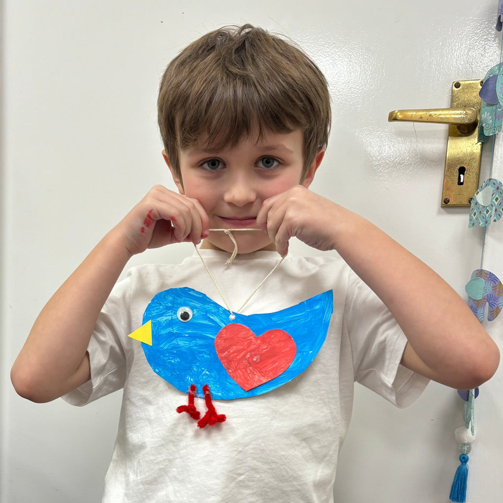 little boy holding his love bird he made at pom stitch tassel craft club.
