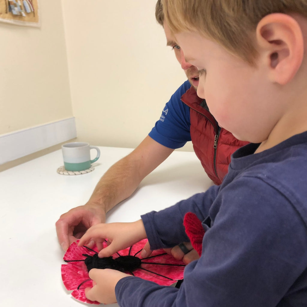 little boy making a paper plate poppy with his dad at little crafters preschool club.
