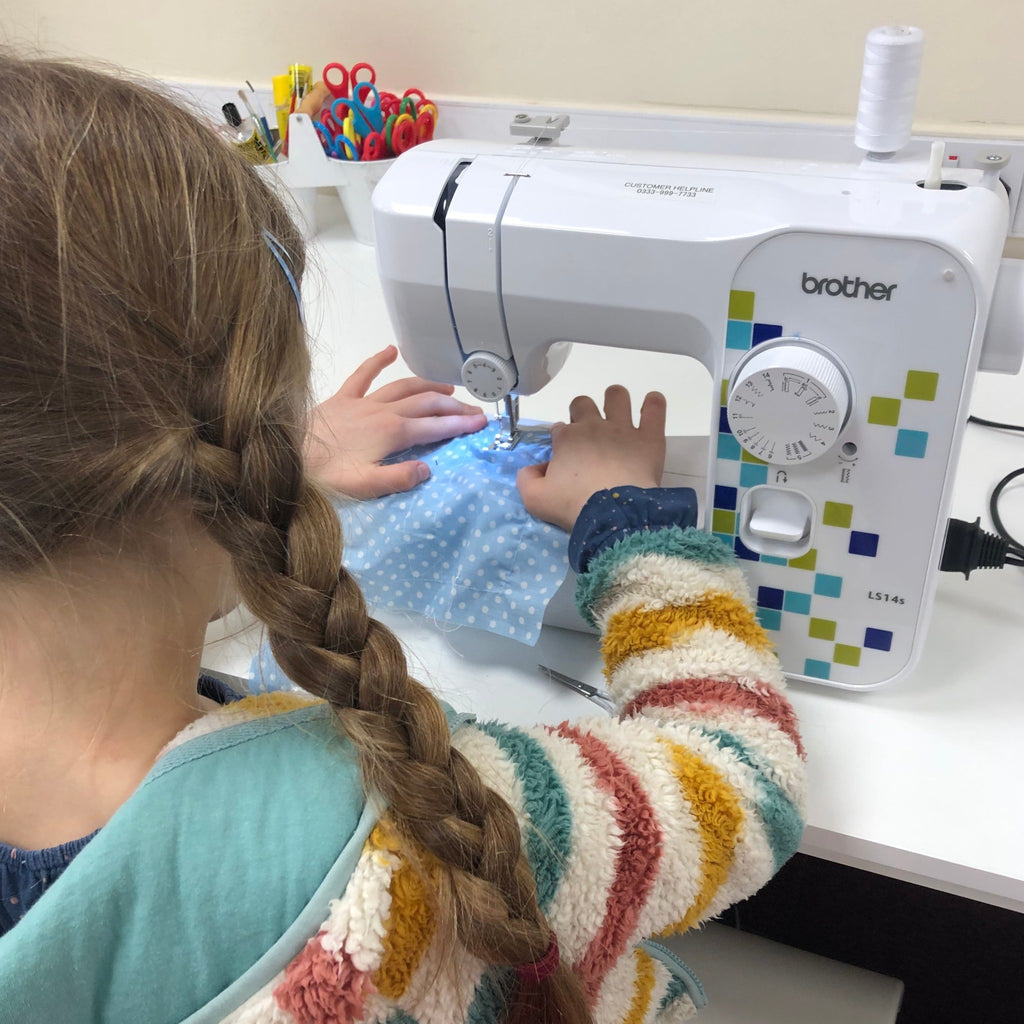 little girl learning to sew on sewing machine with scissors, glue in background.