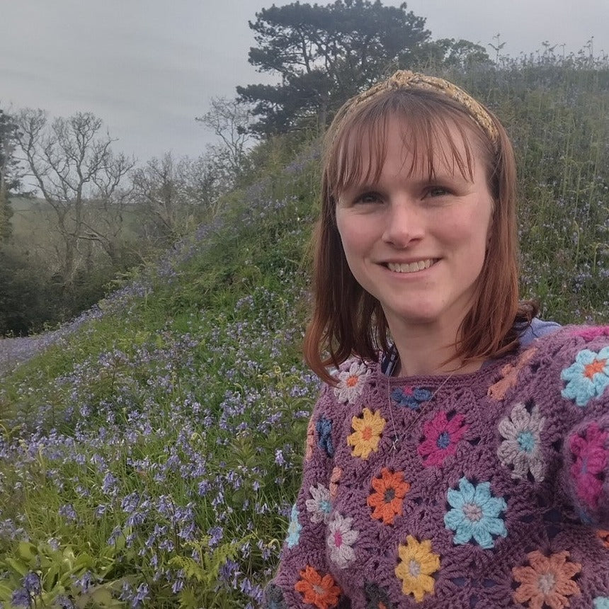 helen from happy devon crochet with crochet jumper and field with bluebells in background.