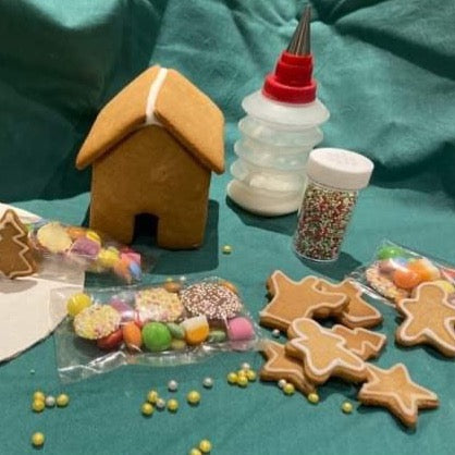 Gingerbread house with icing, sweets and gingerbread biscuits on a green background.