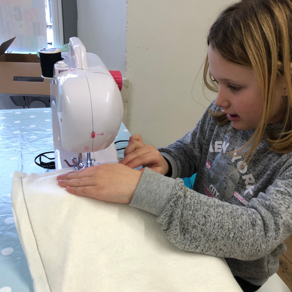 Young girl learning to sew on her sewing machine. Sewing a seam on white fabric.