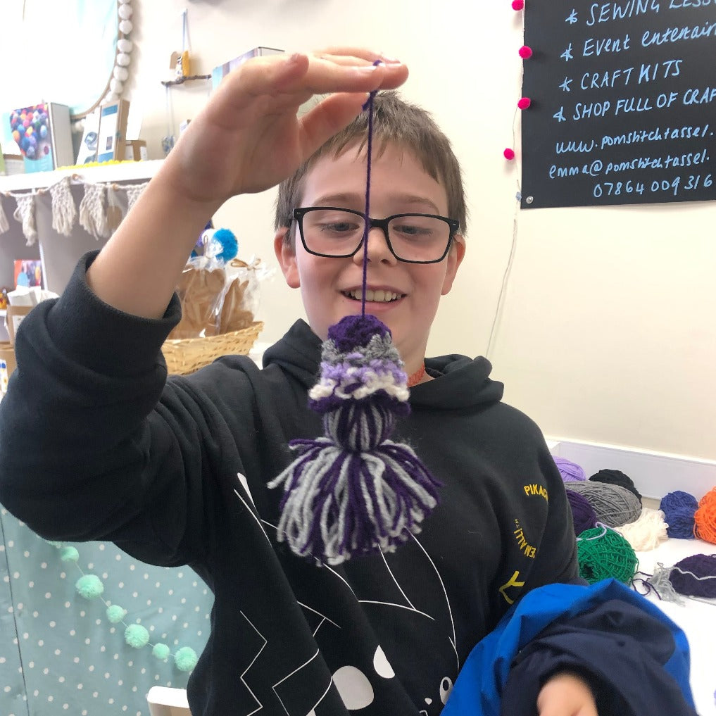little boy showing his crochet decoration with tassel. Grey and purple decoration created in saturday crochet club at pom stitch tassel HQ.