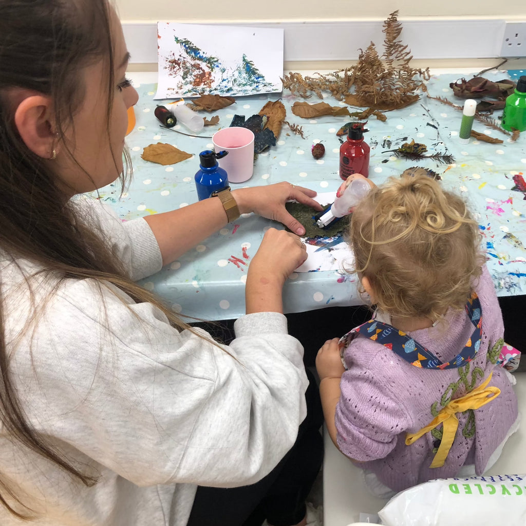 little girl and her mum enjoying little crafters pre school club at pom stitch tassel. Messy craft table with leaves paint, glue, paper.