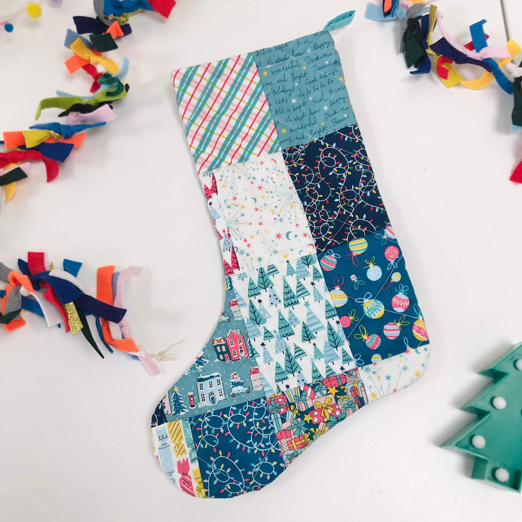 Patchwork stocking on white table with felt garland and christmas tree lights - sewing workshop with pom stitch tassel.