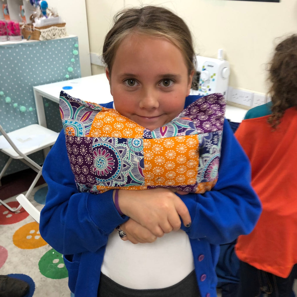 young girl squeezing her patterned cushion she made at stitch club with poms stitch tassel.