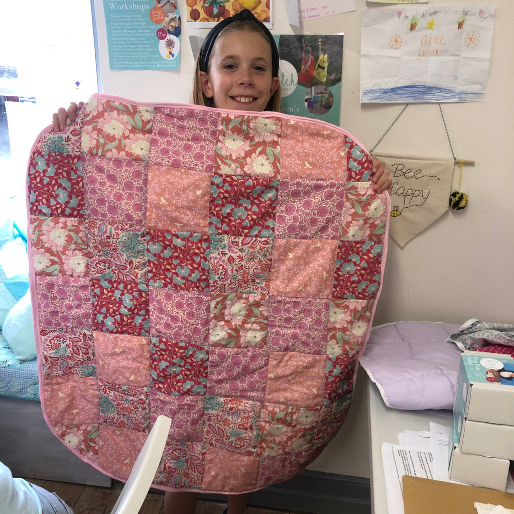 young girl showing off her pink patterned quilt she made at stitch club.