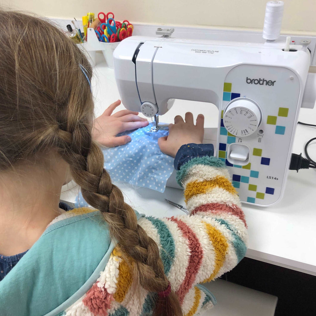 Little girl in striped jumper and plaits sewing fabric on brother sewing machine 