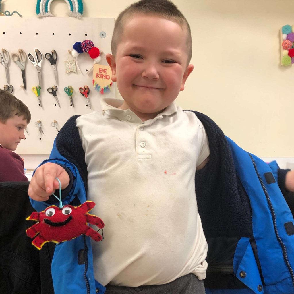 Smiley young lad holding his spider craft. A red sewn spider.