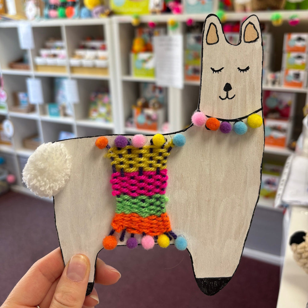 Wooden bolsa Llama with multi colour weaved blanket and pom pom trim. Shop in background