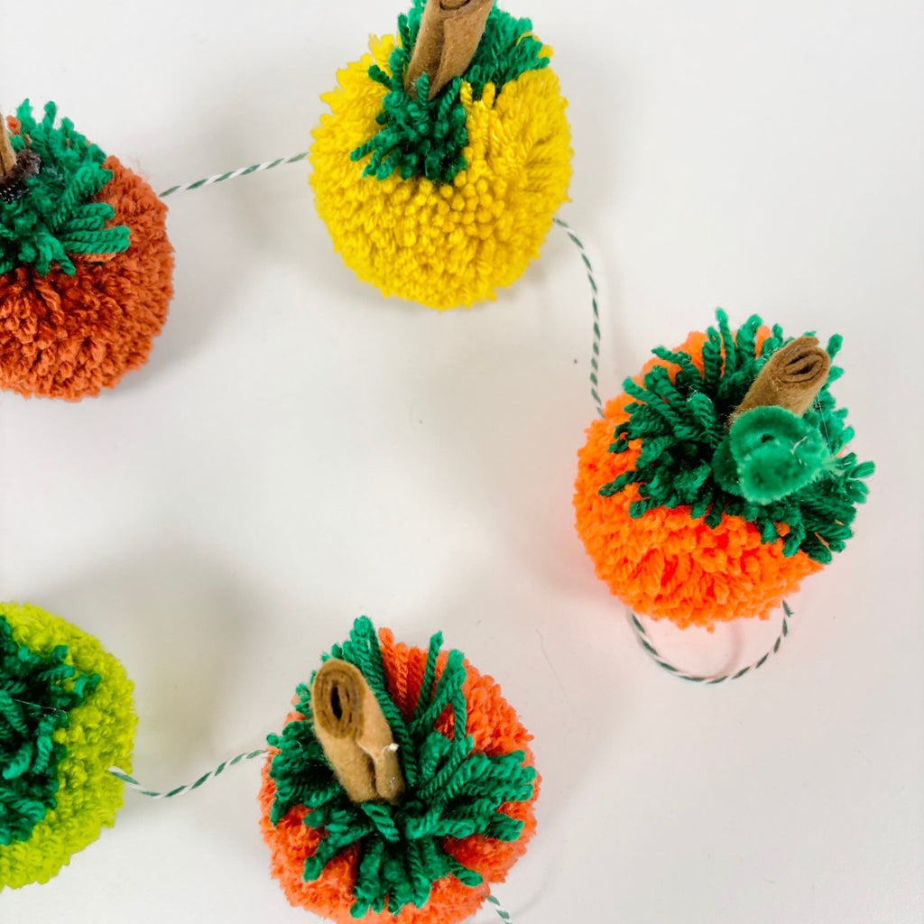 pom pom pumpkins on green bakers twine to make a pumpkin garland