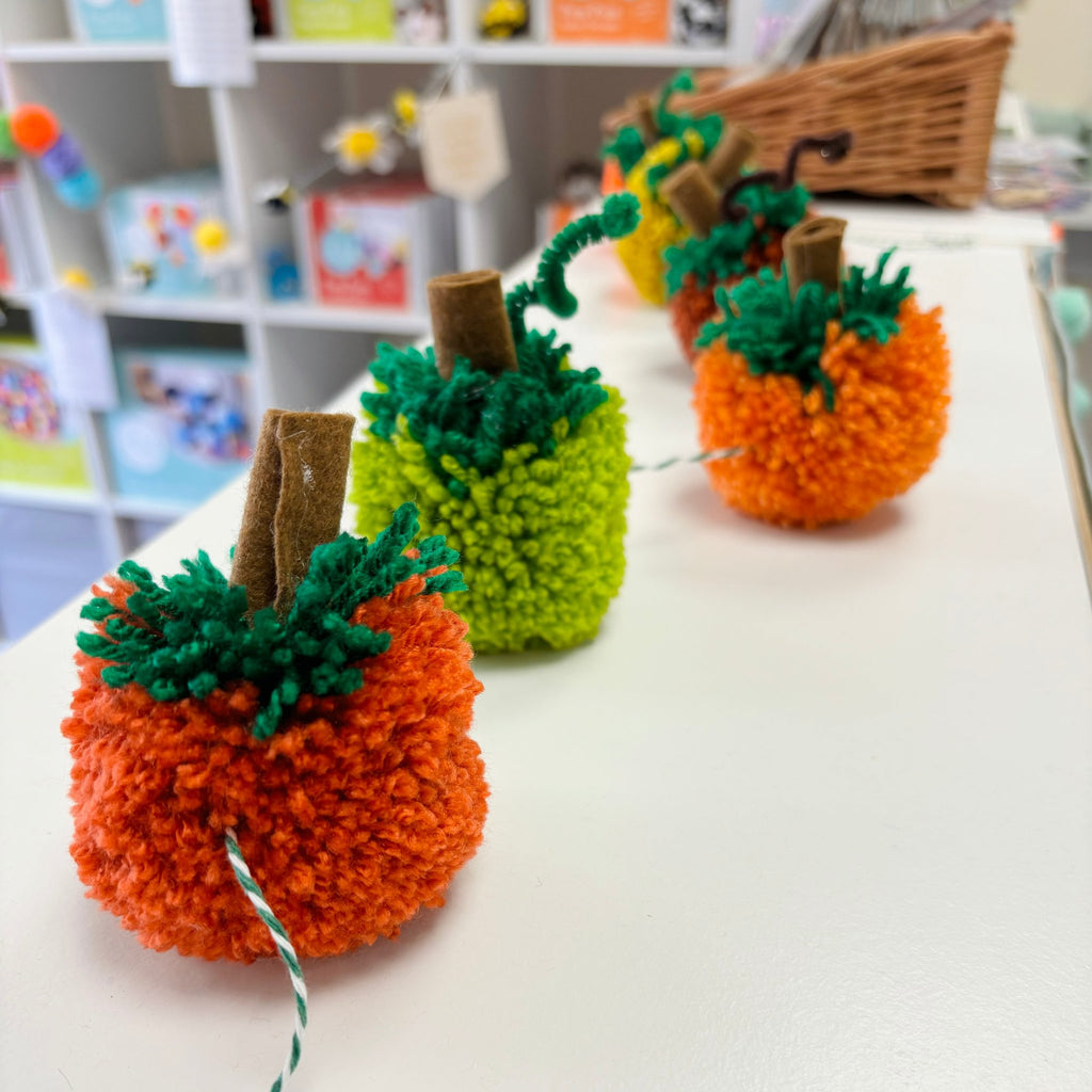 Pumpkin garland on white shelf. Orange, green, yellow pom pom pumpkins with brown felt stalks and pipe cleaner climbers.