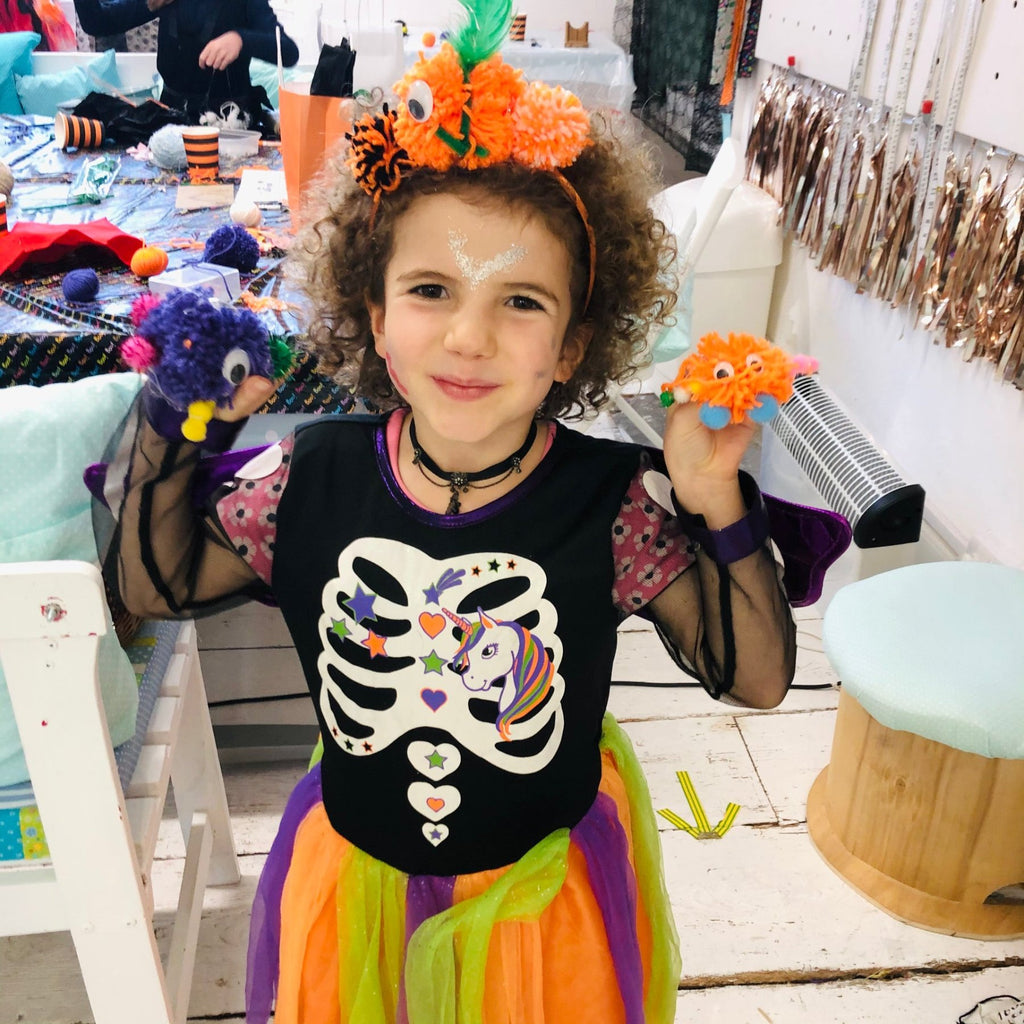 Little girl dressed as a skeleton with pom pom pumpkin headband