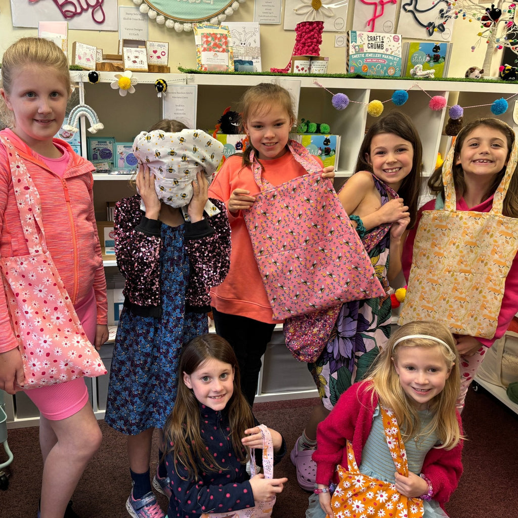 young girls showing their patterned tote bags they made at a pom stitch tassel sewing party
