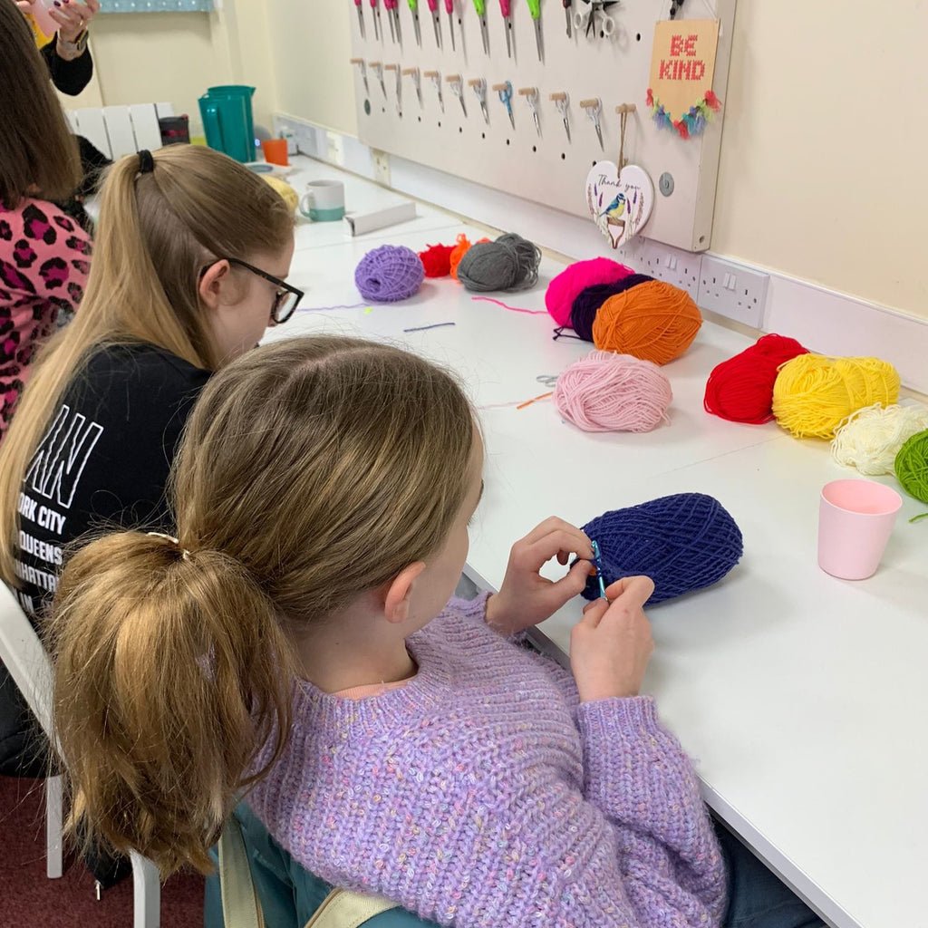 Two young girls learning to crochet at Pom stitch tassel Hq.