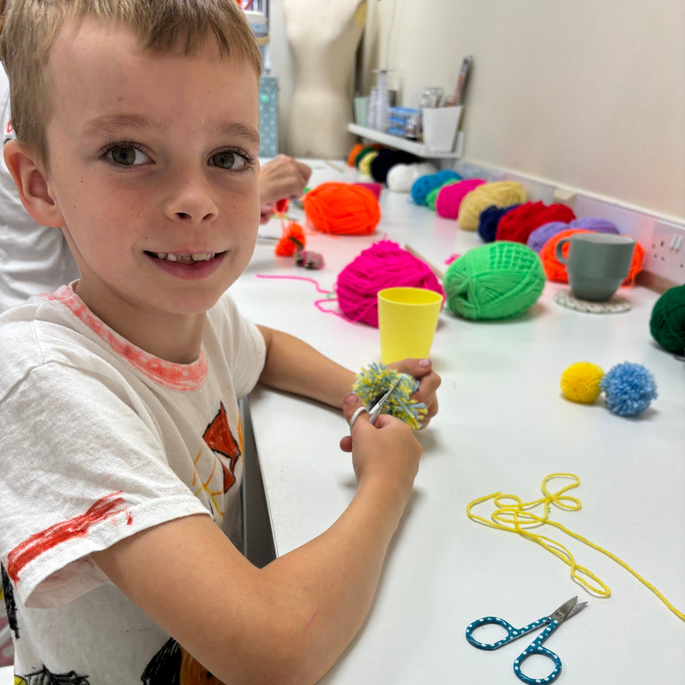 little boy making pom poms - cutting a sprinkle pom with scissors.