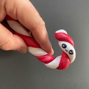 candy cane with smiley face in hands on grey background.