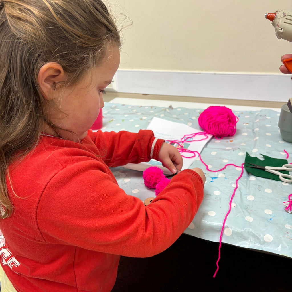 little girl making pink pom poms