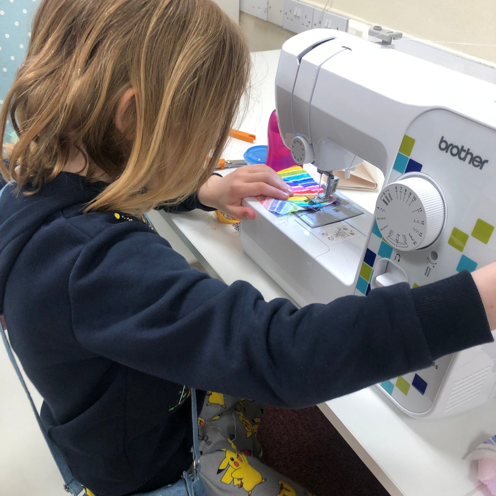 little girl using brother sewing machine to sew rainbow fabric - sewing party