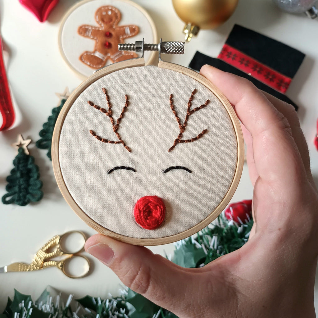 reindeer embroidery hoop in hands with crafting creations and tools behind.