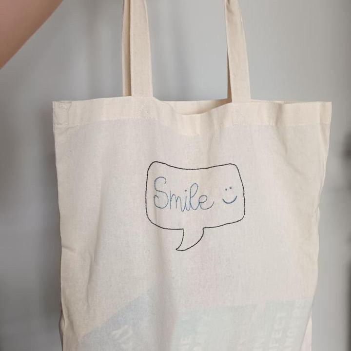 tote bag embroidered with smile on grey background.