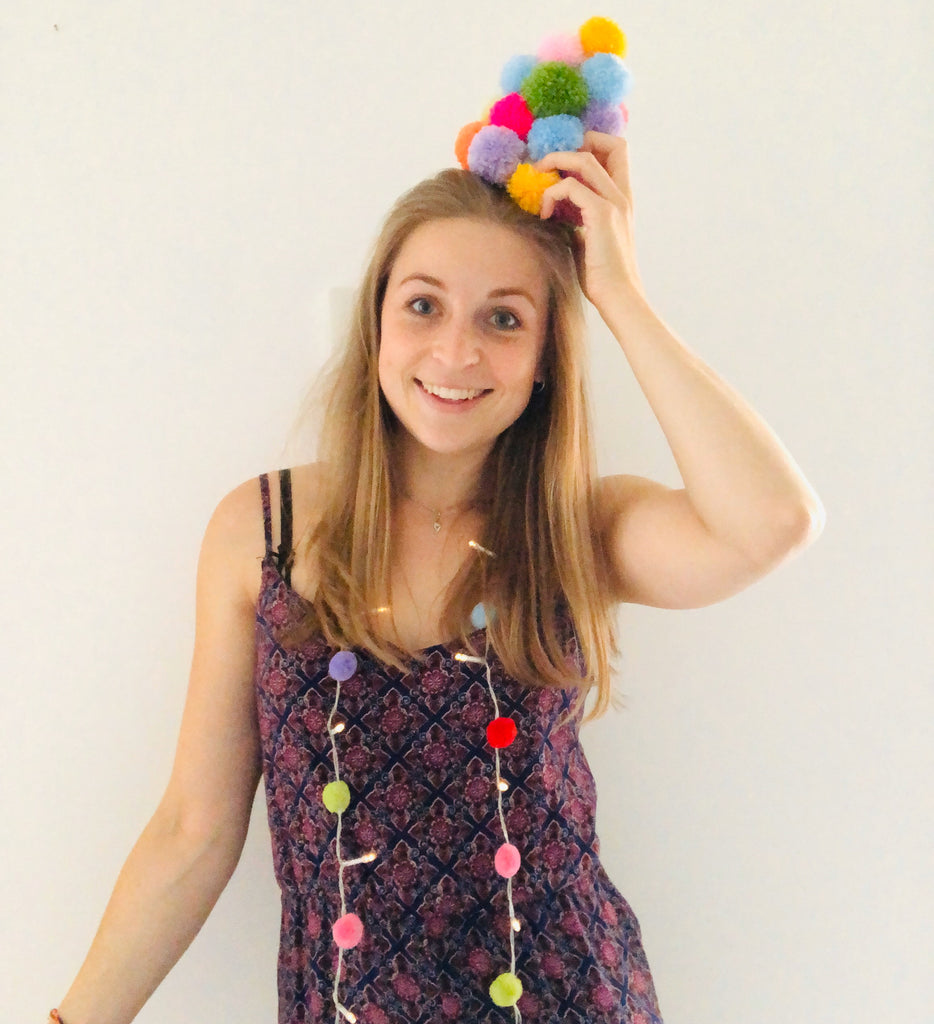 emma with pom pom tree on head! in patterened jumpsuit with white background.