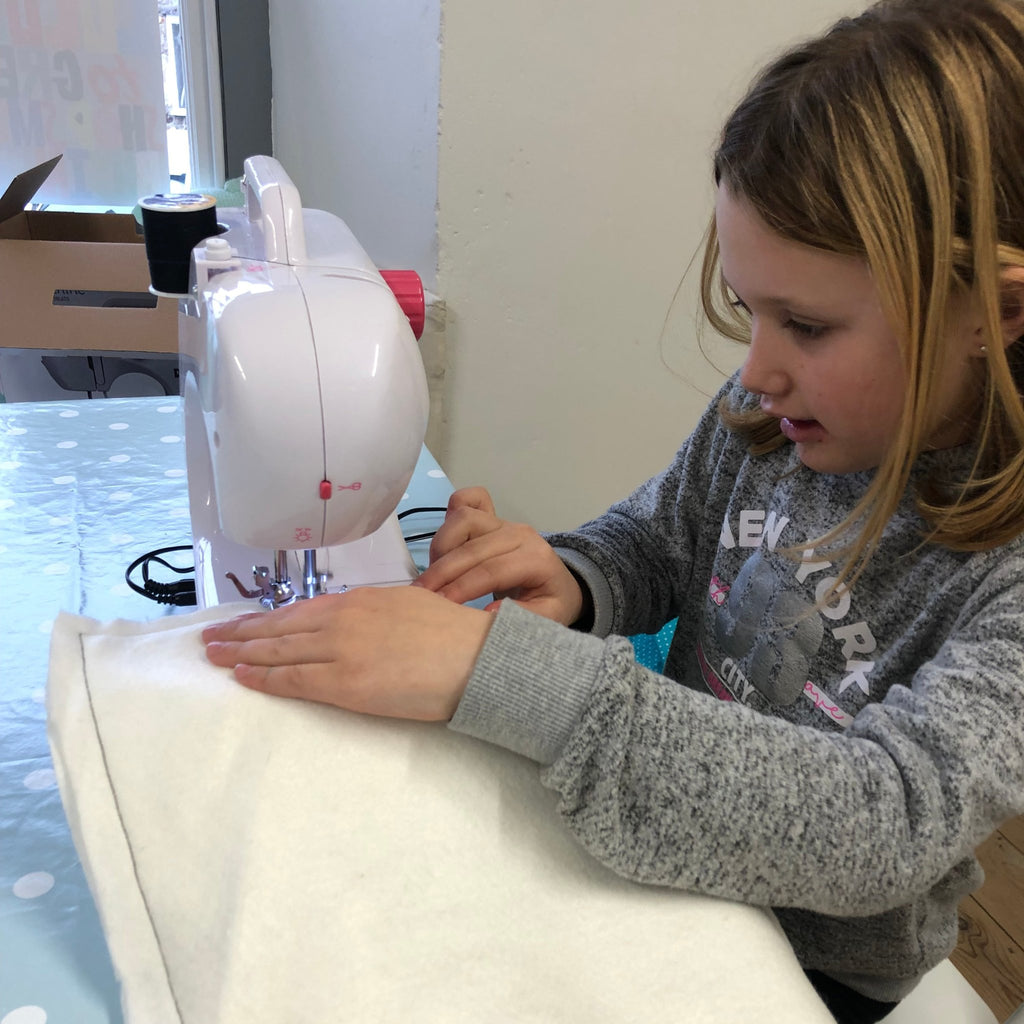 darcey learning to sew on a sewing machine with white fabric and black stitching