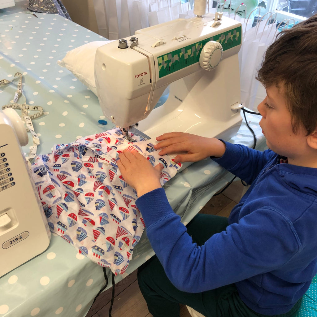 Young lad sewing nautical fabric at a table. Patterned table cloth on table.